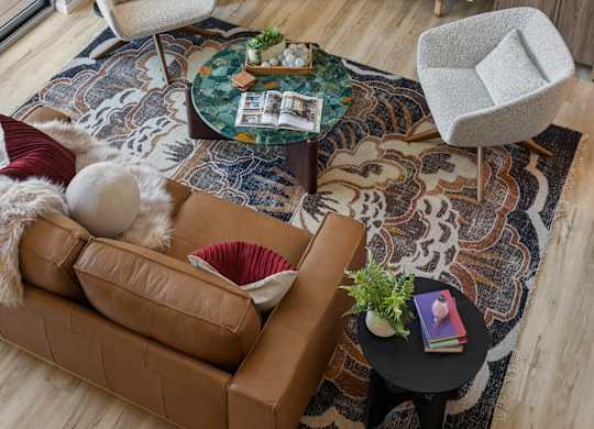 View from a loft unit at The Ellory. A living room with a brown couch, a white chair, and a rug with a pattern.