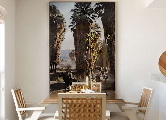 A dining room with a table set for two and a large painting of a palm tree in the background at The PARKER on E Mulberry Apartments, Texas