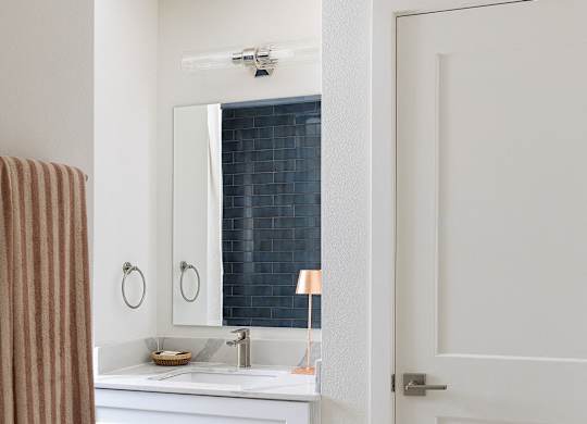 A bathroom with a white door and a white sink with a brown towel hanging on the wall at The PARKER on E Mulberry Apartments, San Antonio, TX, 78209