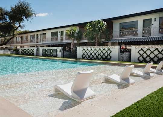 A row of white lounge chairs are arranged on the edge of a pool at The PARKER on E Mulberry Apartments, San Antonio, 78209