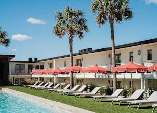 A row of lounge chairs are set up under red umbrellas on a lawn at The PARKER on E Mulberry Apartments, San Antonio