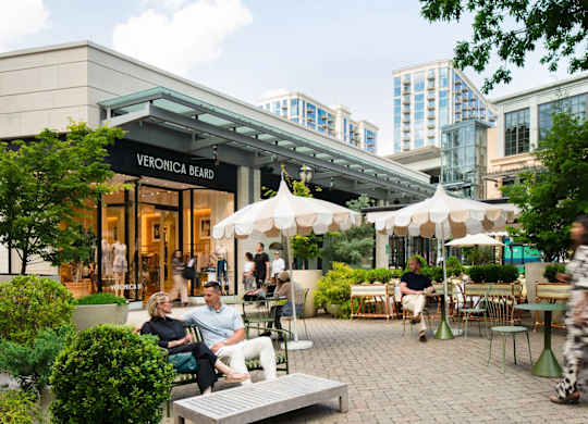 A woman is sitting on a bench outside of a Veronica Beard store.