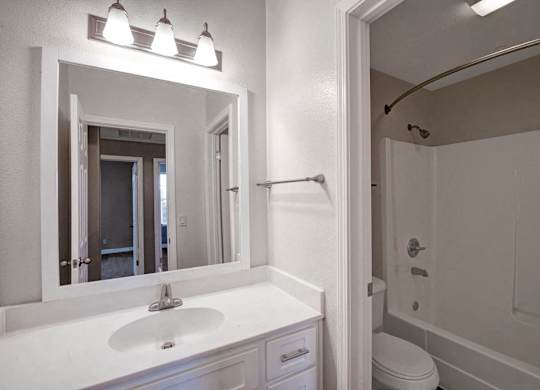A white bathroom with a sink, mirror, and toilet.