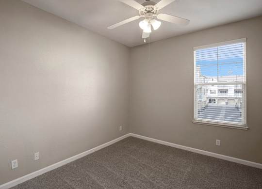 A room with a ceiling fan and a window overlooking a parking lot.