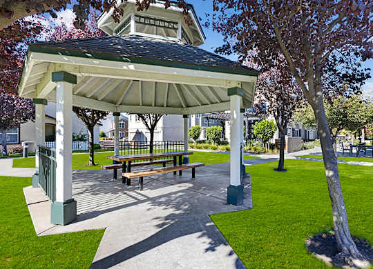 A gazebo with a bench is surrounded by a green lawn.
