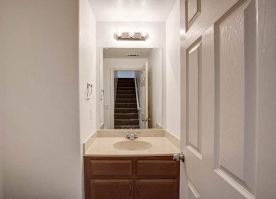 A bathroom with a sink, toilet, and a staircase in the background.