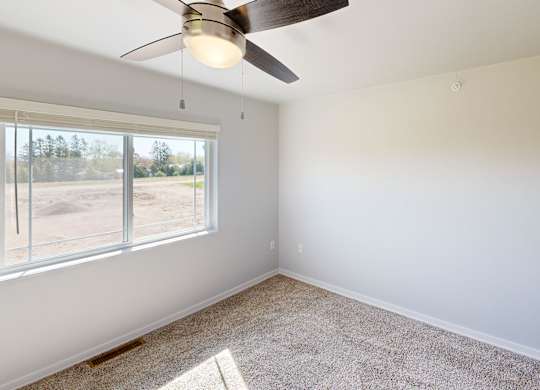 A room with a ceiling fan and a window overlooking a parking lot.