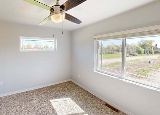 A room with a ceiling fan and two windows.