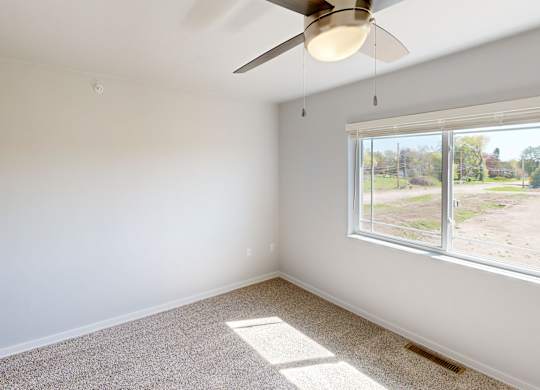 A room with a ceiling fan and a window overlooking a field.