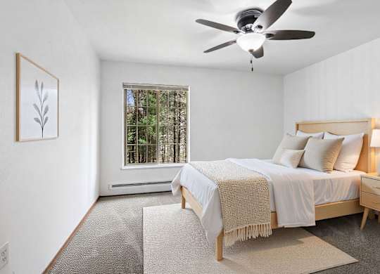 A bedroom with a bed, a ceiling fan, and a window with a view of trees.