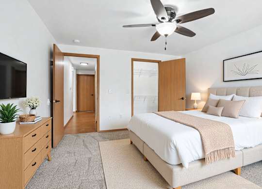 A bedroom with a large bed, a ceiling fan, and a TV on the wall.