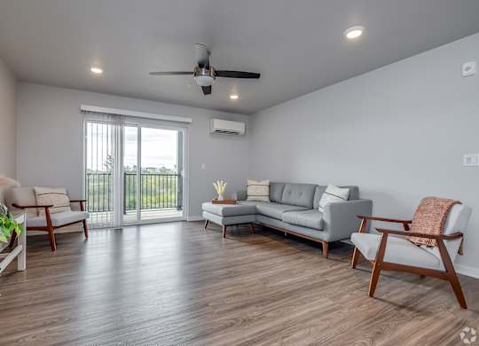 A living room with a grey sofa, wooden chairs, and a ceiling fan.
