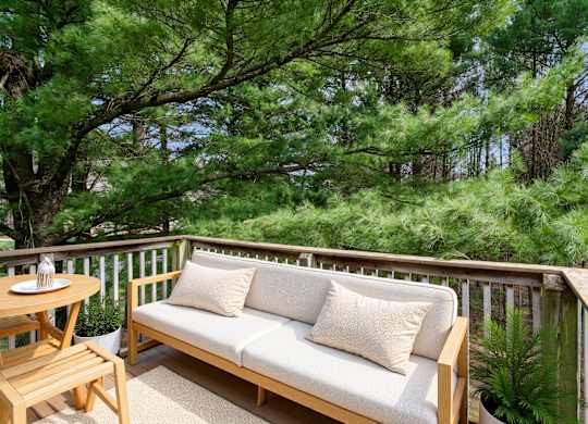 A wooden bench with cushions is on a balcony with a table and chairs.