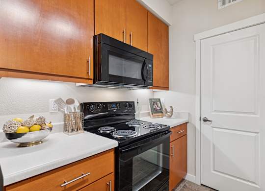 A kitchen with a black microwave above a stove and wooden cabinets.