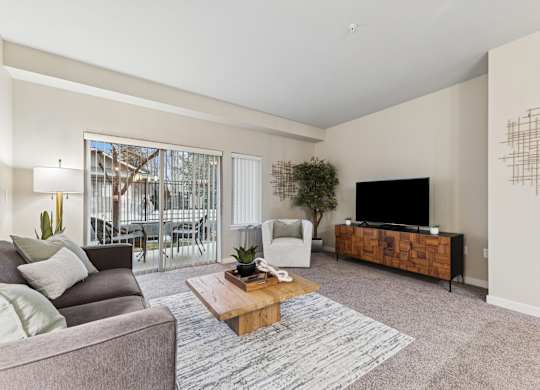A living room with a grey couch, a wooden coffee table, a flat screen TV and a large window.