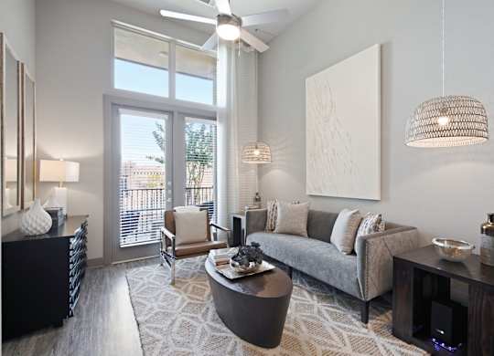 A modern living room with a grey sofa, a wooden coffee table, and a large window with a view of the outside.