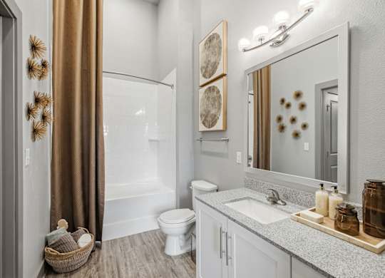 A bathroom with a white toilet, a sink, a mirror, and a shower.