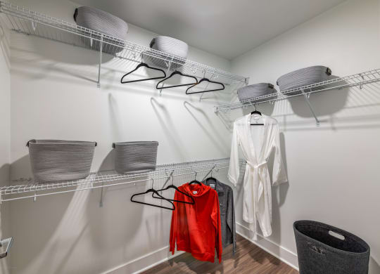 a walk in closet with two wire racks and a white robe and a red jacket