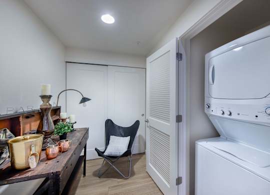 A laundry room with a washing machine and a chair.