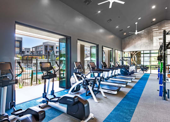 a gym with cardio equipment and windows with a view of a building