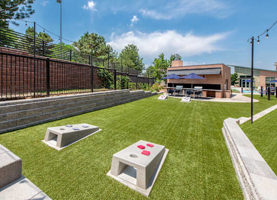 A sunny day at a park with a fence, a building, and a few concrete blocks with red buttons.