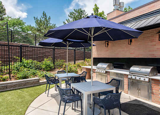 A blue umbrella shades a table with chairs outside.
