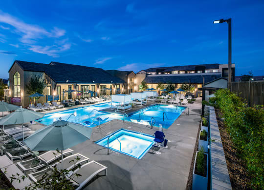 a swimming pool with chairs and umbrellas at night