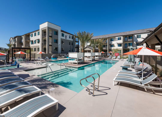 a pool with lounge chairs and umbrellas in front of an apartment building