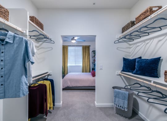 a walk in closet with a bedroom in the background and shelves with clothes on them