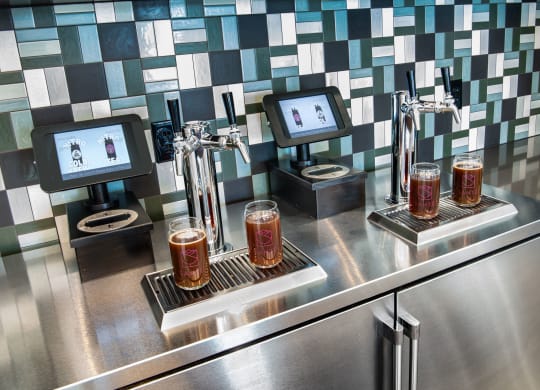 a bar with three glasses of beer on a stainless steel counter