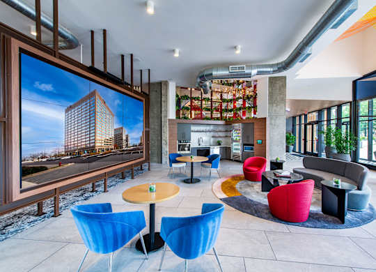 A large screen in a room with blue chairs and a yellow table.