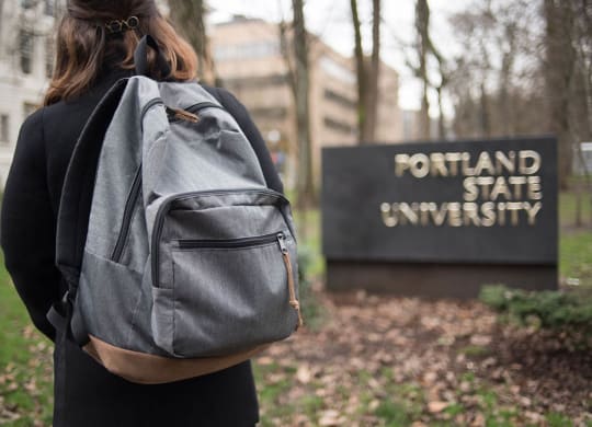 a woman with a backpack standing in front of the fountain state university sign