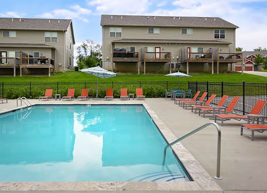 A swimming pool surrounded by red chairs and apartment buildings in the background.
