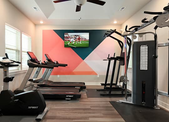 A gym with treadmills, elliptical machines, and a television playing a football game.