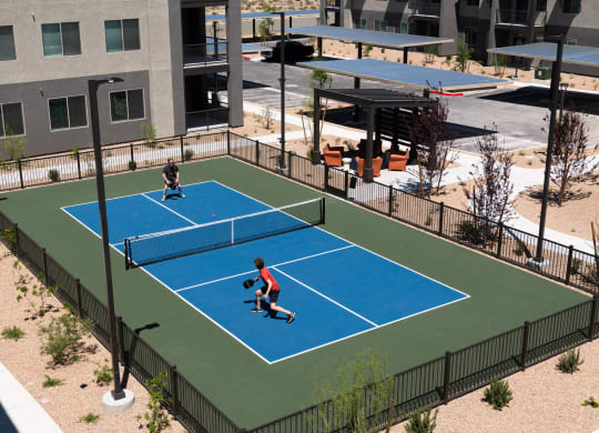 two people playing tennis on a blue court in a park