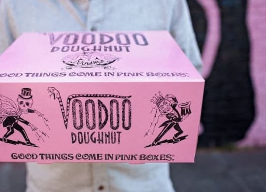a person holding a pink box that says voodoo doughnut