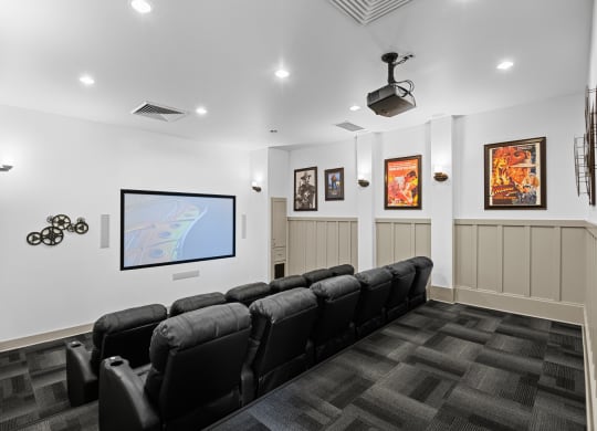 a theater room with a row of black chairs and a tv on the wall