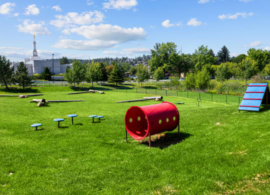 a playground with a seesaw and a red barrel in a field