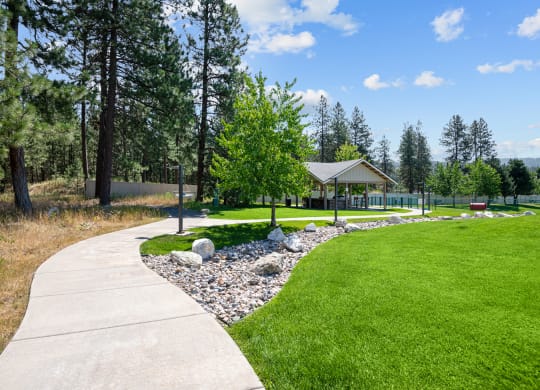 a sidewalk leading to a park with a gazebo and trees