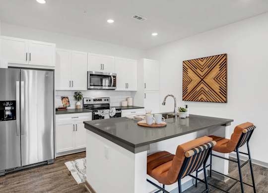 A modern kitchen with a refrigerator, microwave, oven, sink, and bar stools.