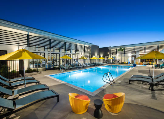 a pool with lounge chairs and umbrellas in front of a building