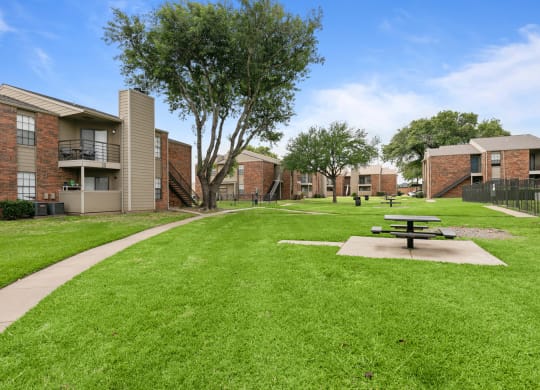 a picnic table sits in the middle of a grassy area in front of a brick building