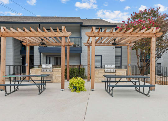 a picnic area with two picnic tables and a barbecue grill in front of a building