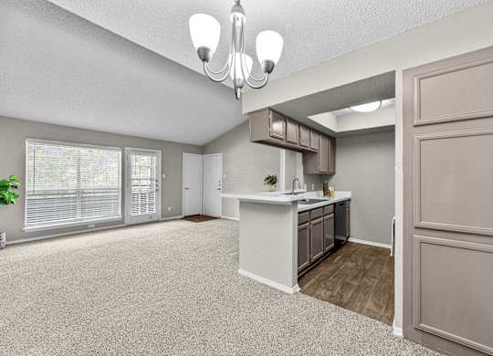 A spacious kitchen and living room with a chandelier and a potted plant.