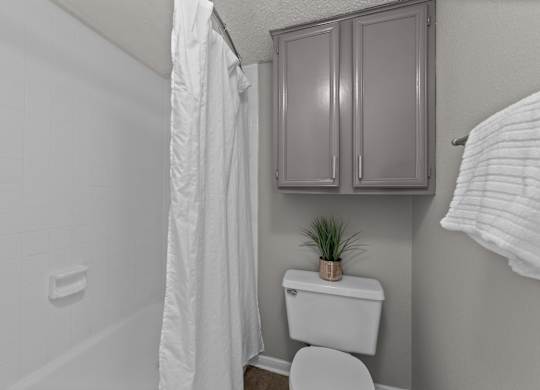 A white toilet sits in a bathroom next to a white shower curtain.