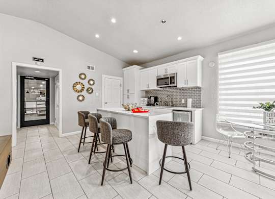 A kitchen with white cabinets and a bar area with stools.