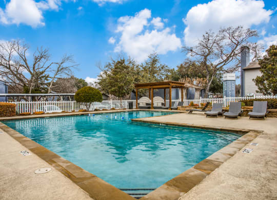 a swimming pool with a gazebo and lounge chairs next to a house