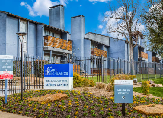 a blue and white sign is in the middle of a garden in front of an apartment building