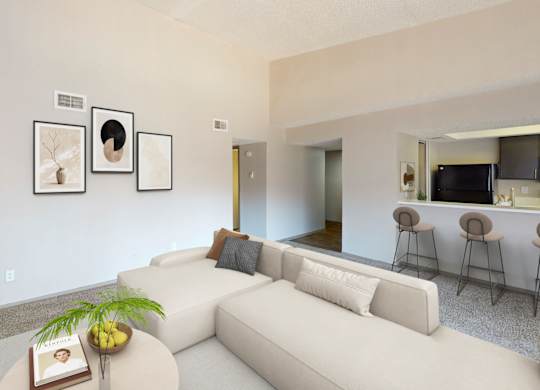 A living room with a white couch, a coffee table with a book and a plant on it, and a wall with three framed pictures.