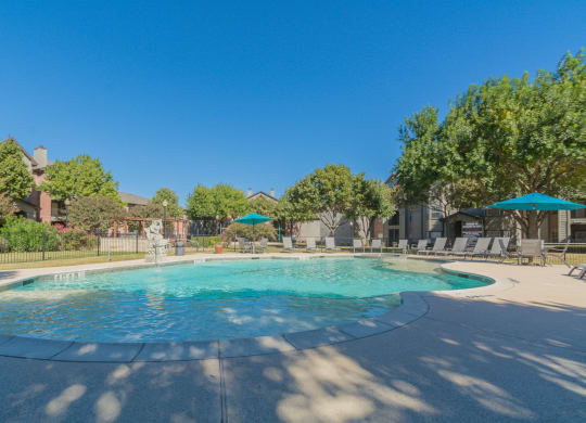 a swimming pool with umbrellas and buildings in the background at Fountains of Denton in Denton, TX